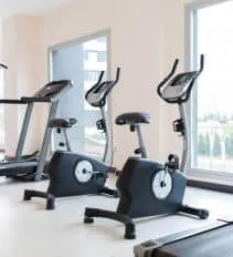 Stationary bikes and treadmills lined up beside the windows of an apartment community fitness room