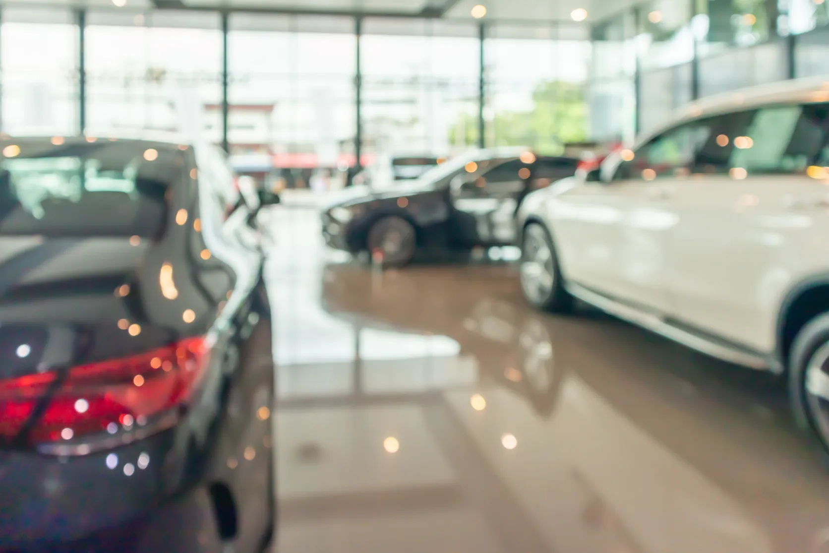 Polished car dealership showroom floor with vehicles on display, reflecting overhead lighting.