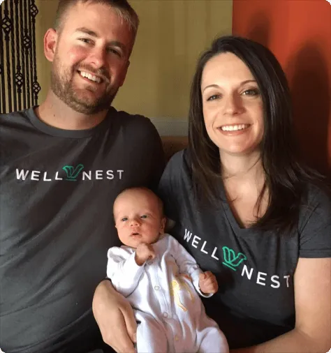Phil and Nicole Harper, founders of WellNest Professional Cleaning, smiling together in WellNest t-shirts while holding their infant child at home