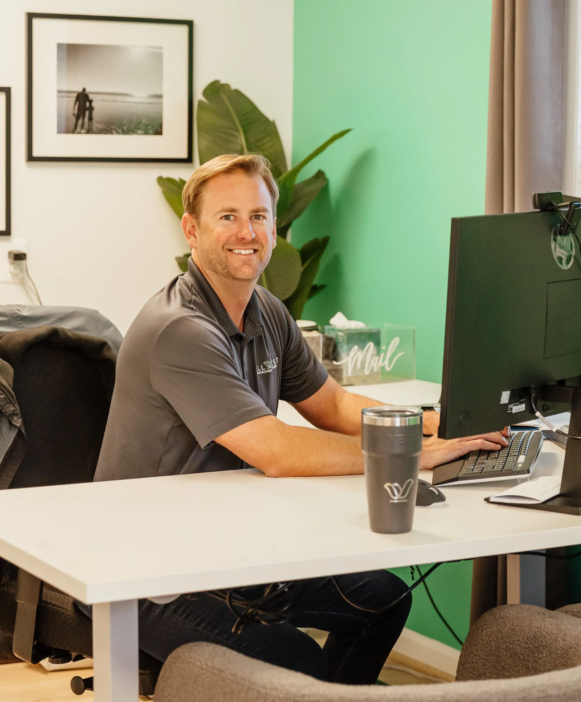 Phil Harper, WellNest's founder, smiling at his desk in the WellNest office with a WellNest tumbler in front of him.