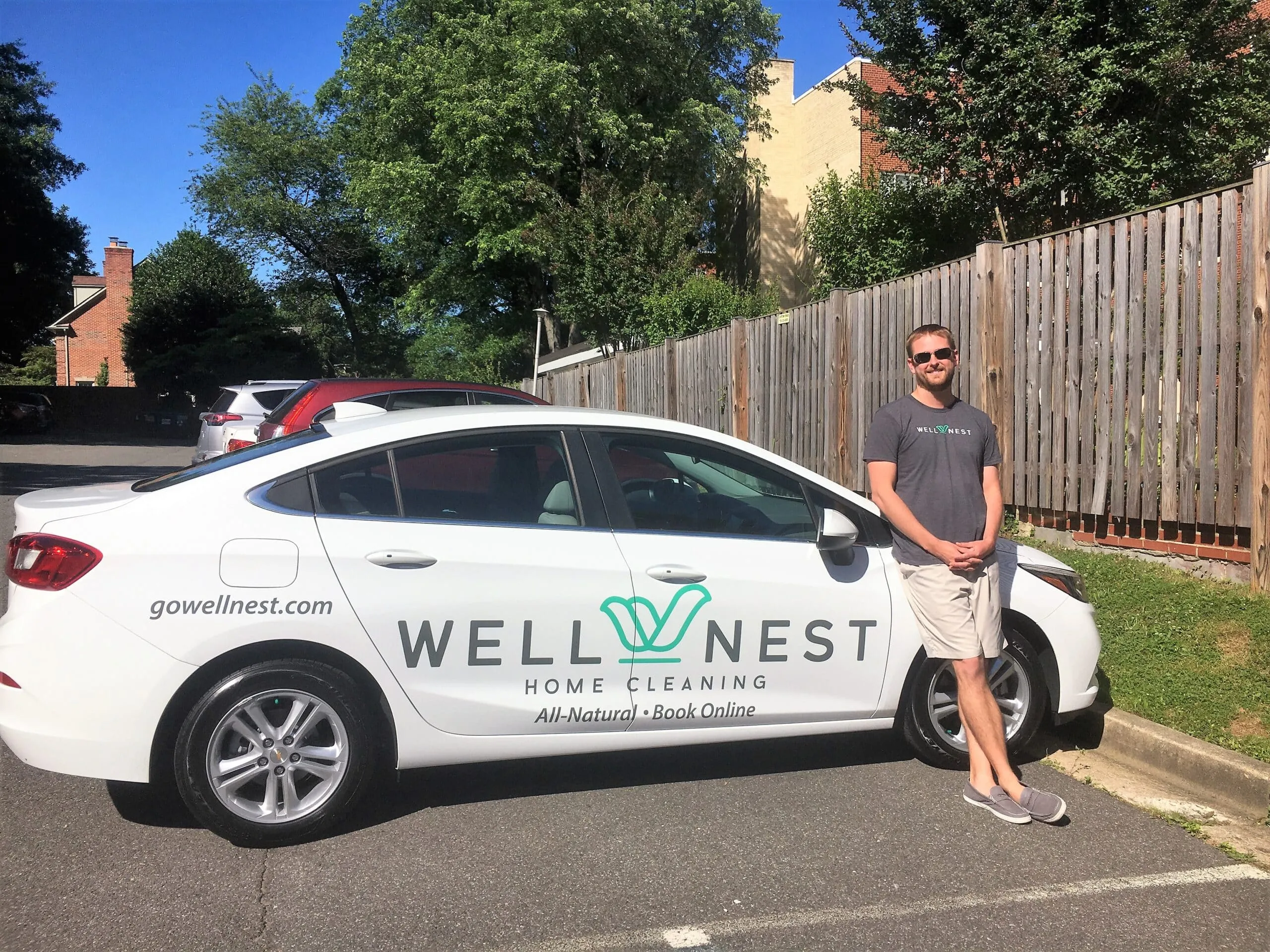 Phil Harper standing beside a white WellNest company car with the logo and gowellnest.com on the door