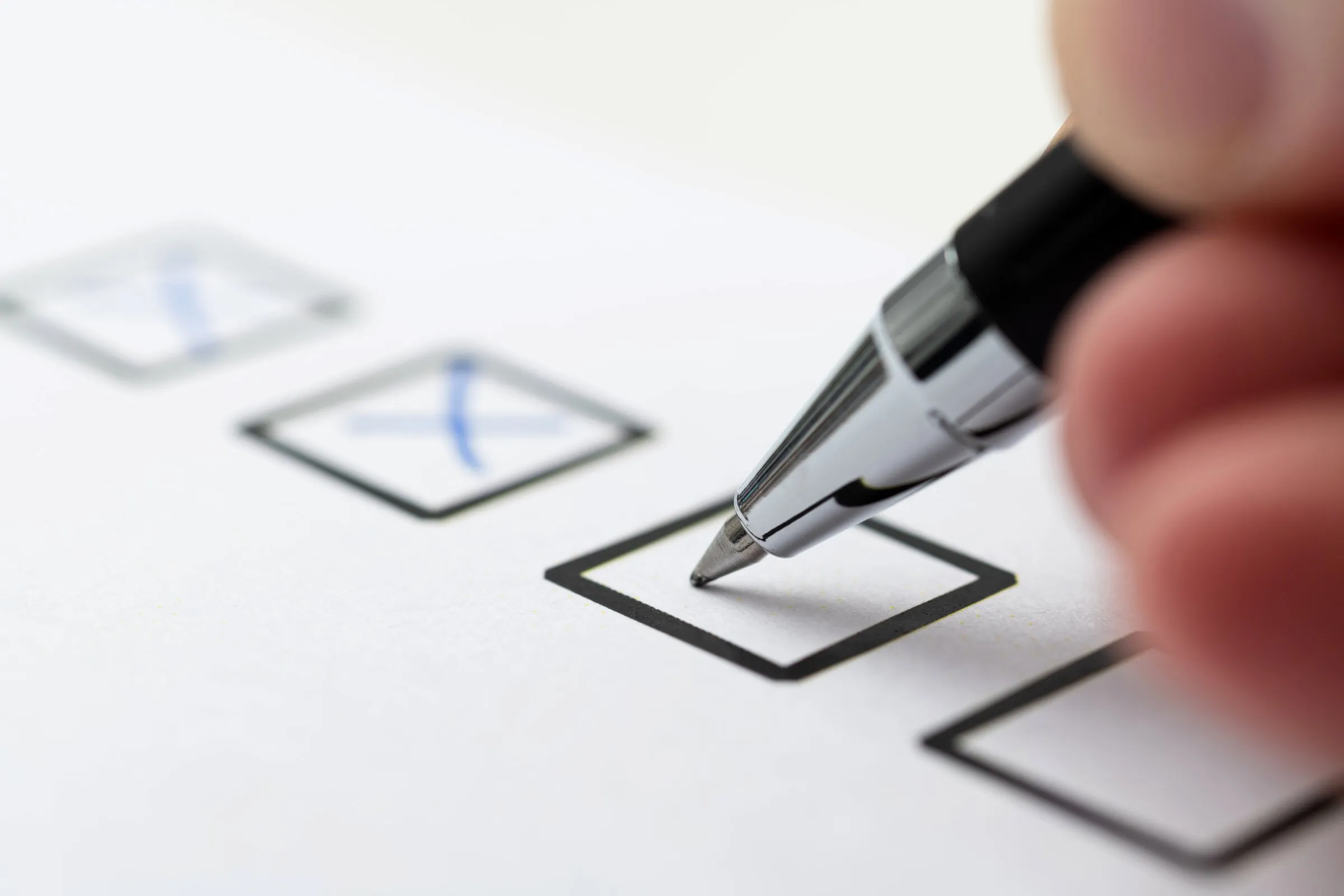 A hand checking off boxes on a printed checklist with a black pen.
