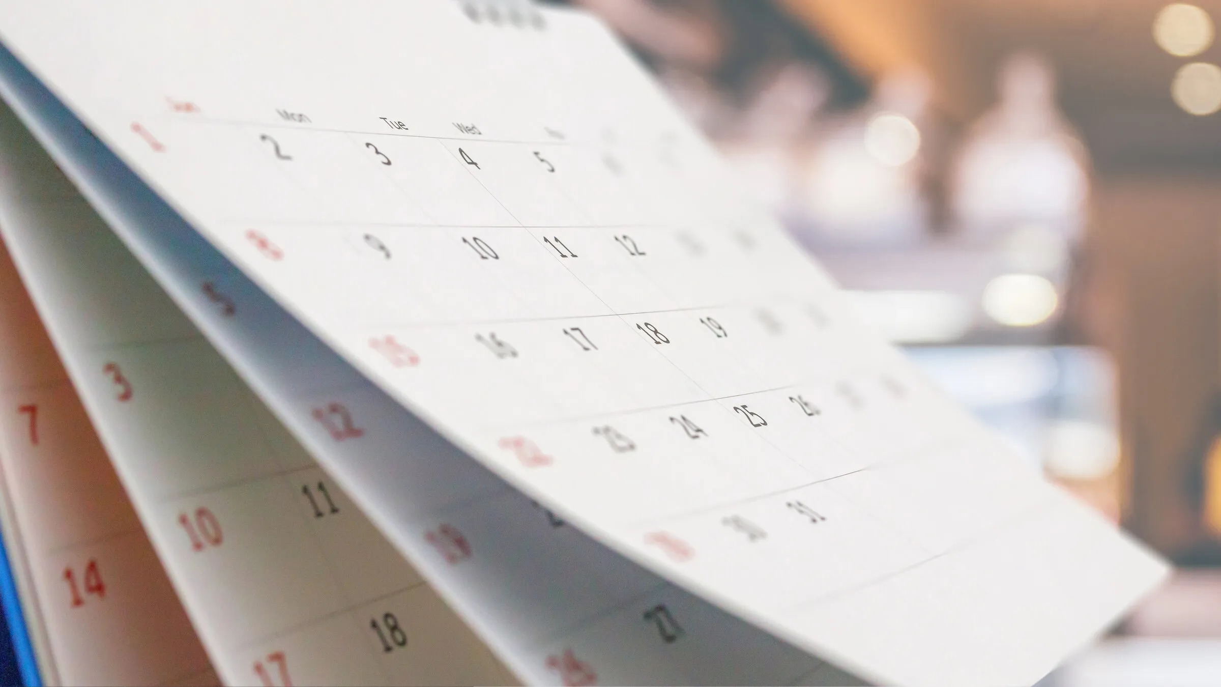 A desk calendar with the month's pages turning, set against a softly lit background.
