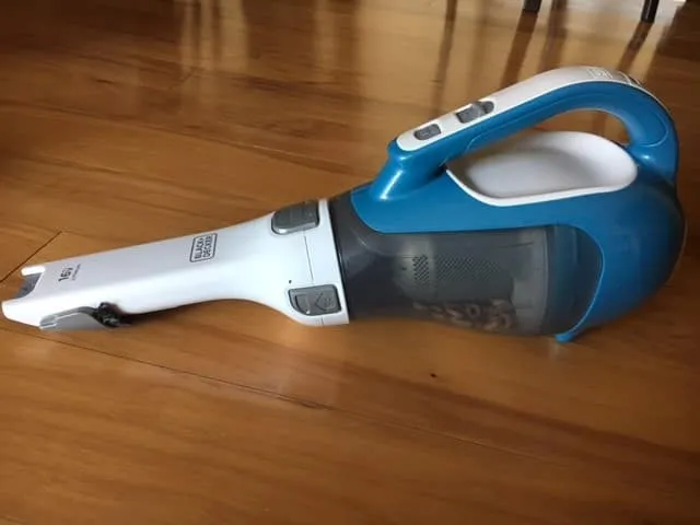 A handheld cordless vacuum on a hardwood floor with cereal visible in its clear dust cup